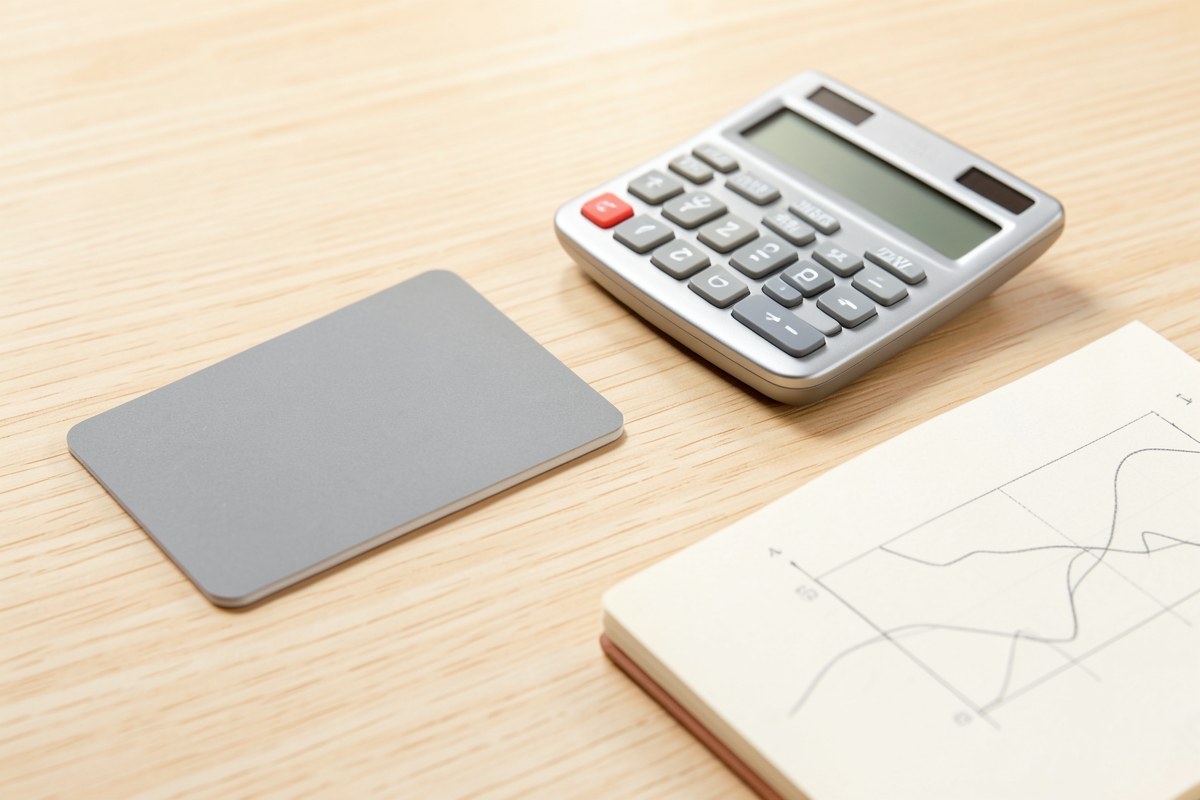 A credit card lying on a desk with a calculator and a notepad showing a simple chart, evoking financial planning and balance transfers.